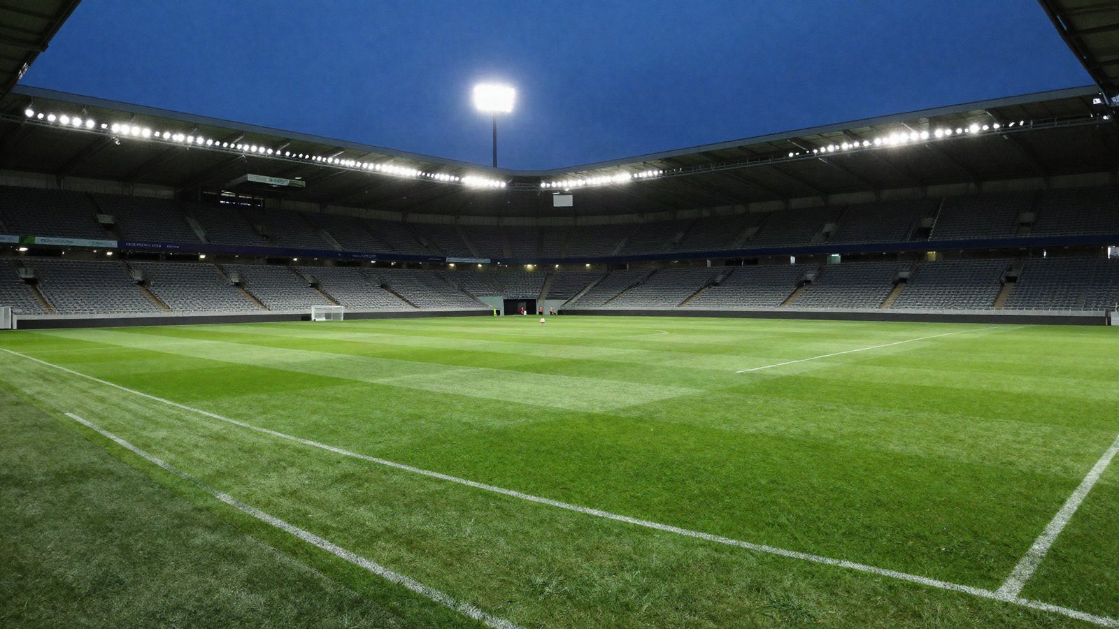 An empty football stadium under floodlights at dusk with a ball on the centre spot